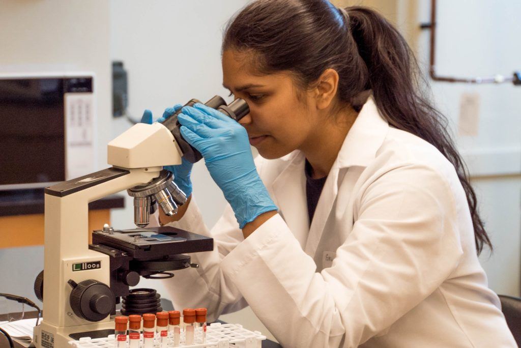 This picture show a girl looking through a microscope.