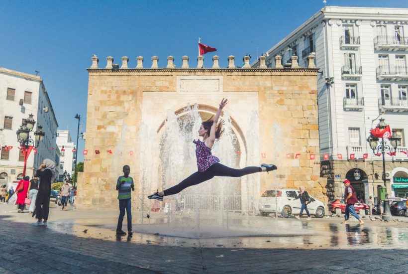 This picture show a person jumping in front of a stone arch.