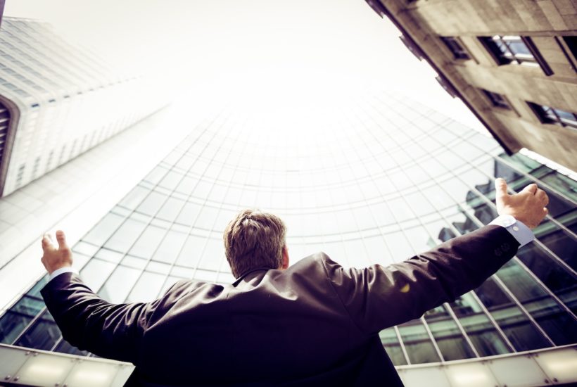 This picture show a person standing on front of a building looking up.