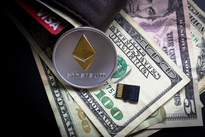 This picture shows a Ethereum coin on top of some dollar bills.