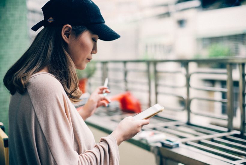 This picture shows a girl using her smartphone while smoking.