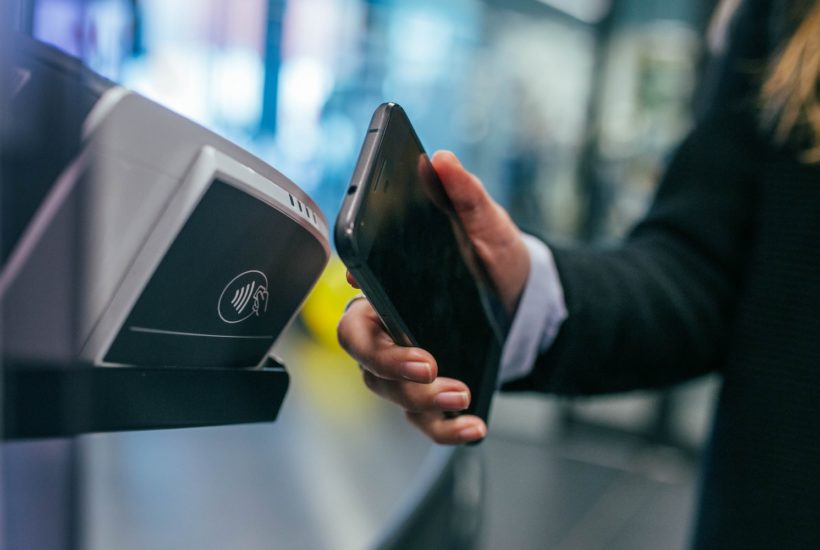 This picture show a woman using her smartphone to pay something.