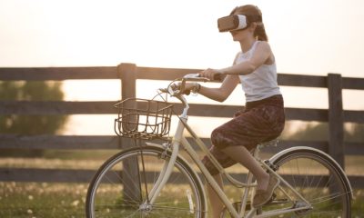 This picture show a woman riding a bike and using a VR set.