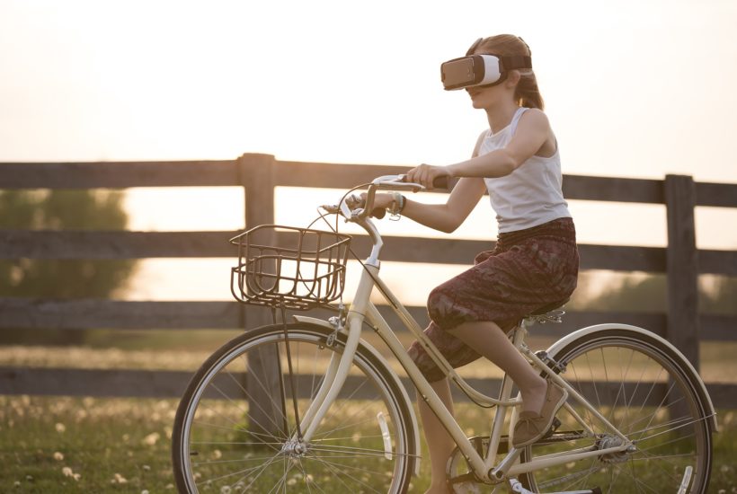 This picture show a woman riding a bike and using a VR set.